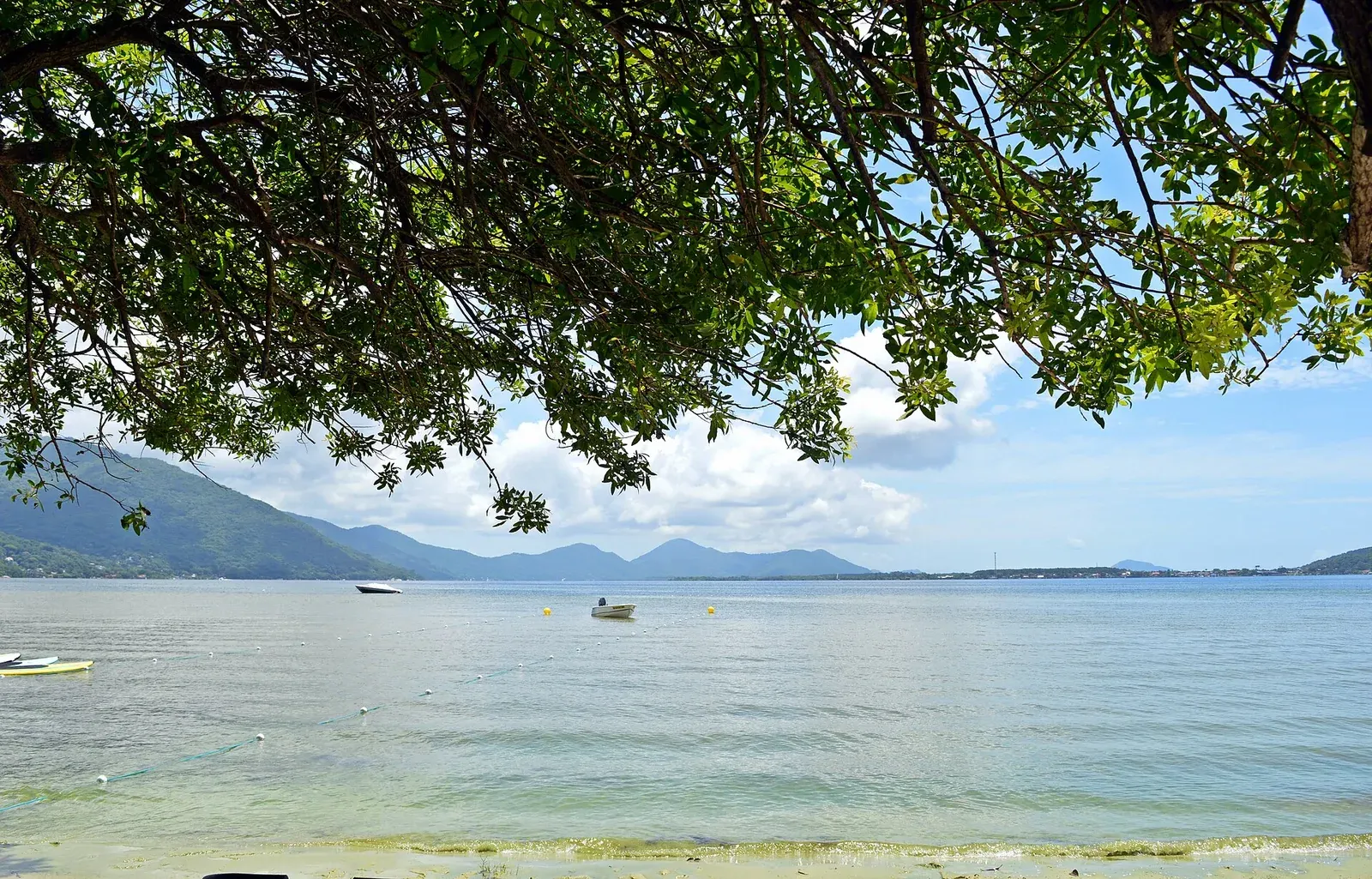 Vista da água calma da Lagoa da Conceição, cercada por morros.